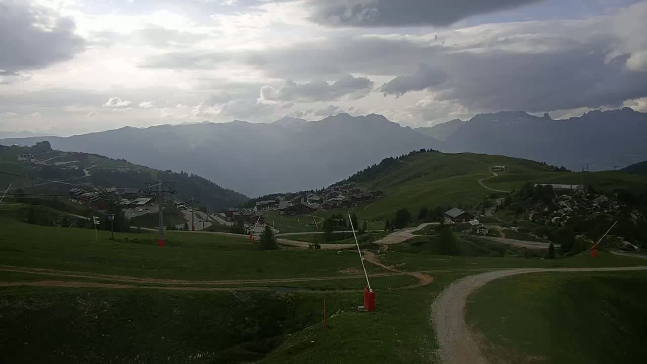A mountainous landscape with a village nestled in a valley under a partly cloudy sky.