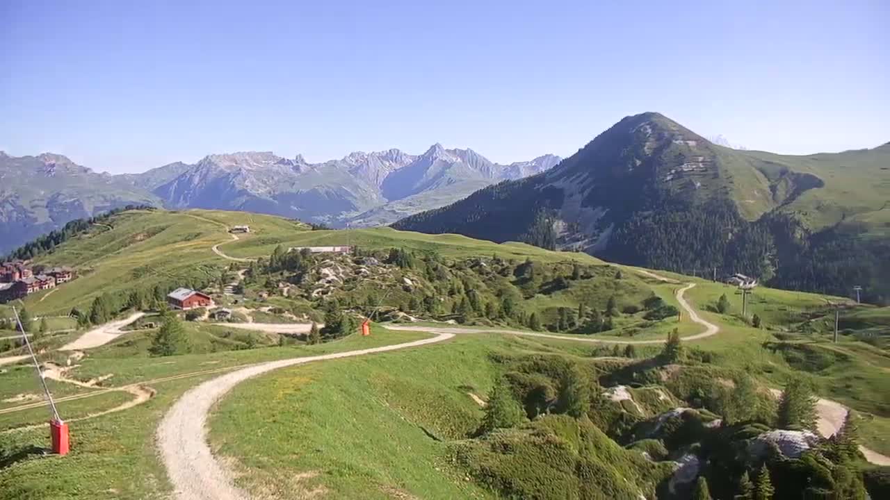A winding dirt road meanders through rolling green hills and mountains under a clear blue sky.