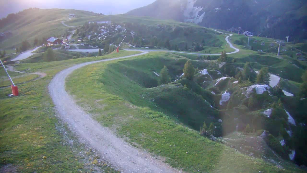 A winding dirt road curves through a grassy mountain landscape under a hazy sky.