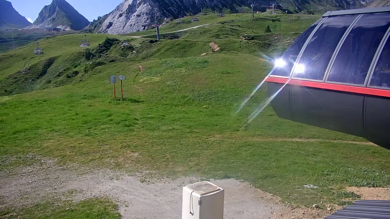 A grassy mountainside with a chairlift in the background and a gondola car in the foreground on a sunny day.