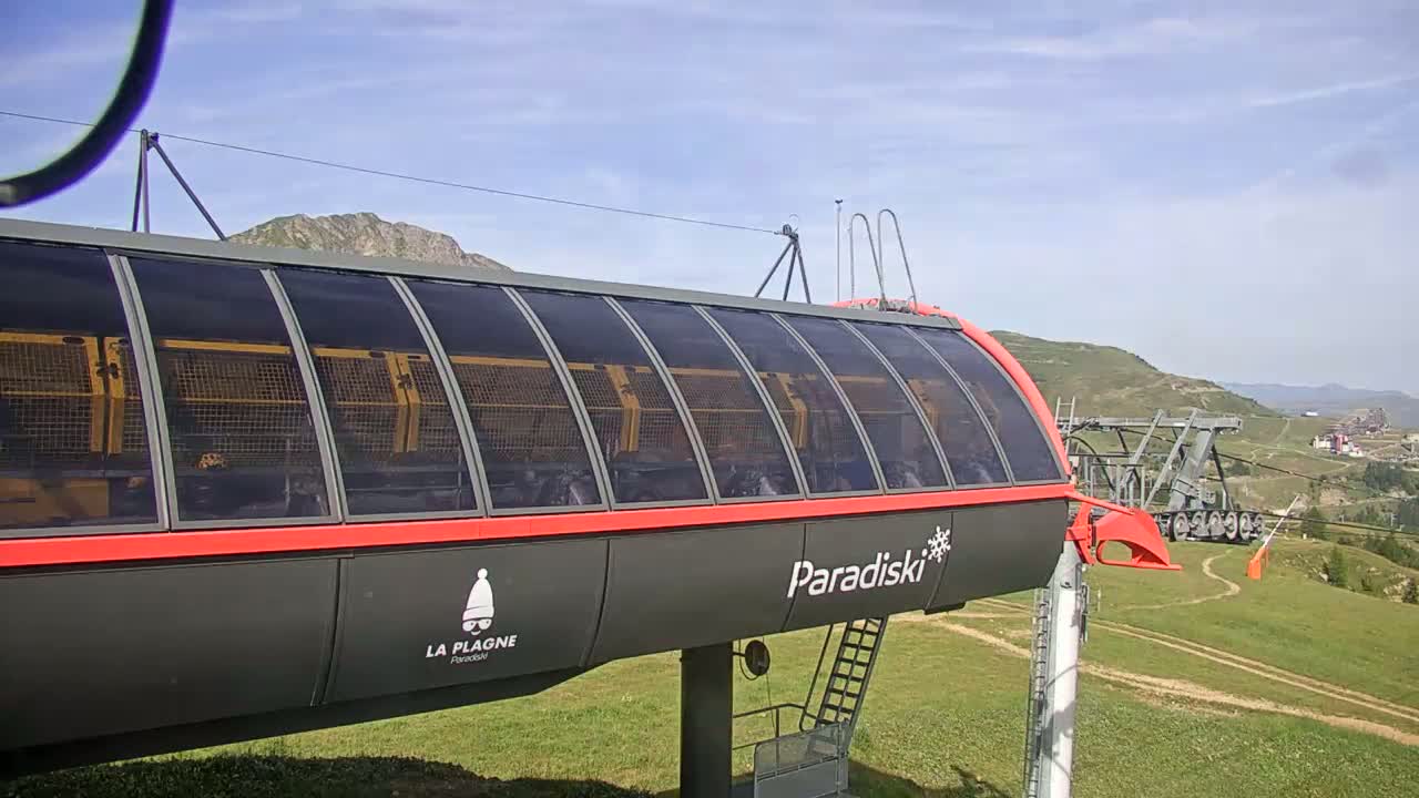 A long, enclosed gondola lift car sits on a grassy hillside under a mostly sunny sky.