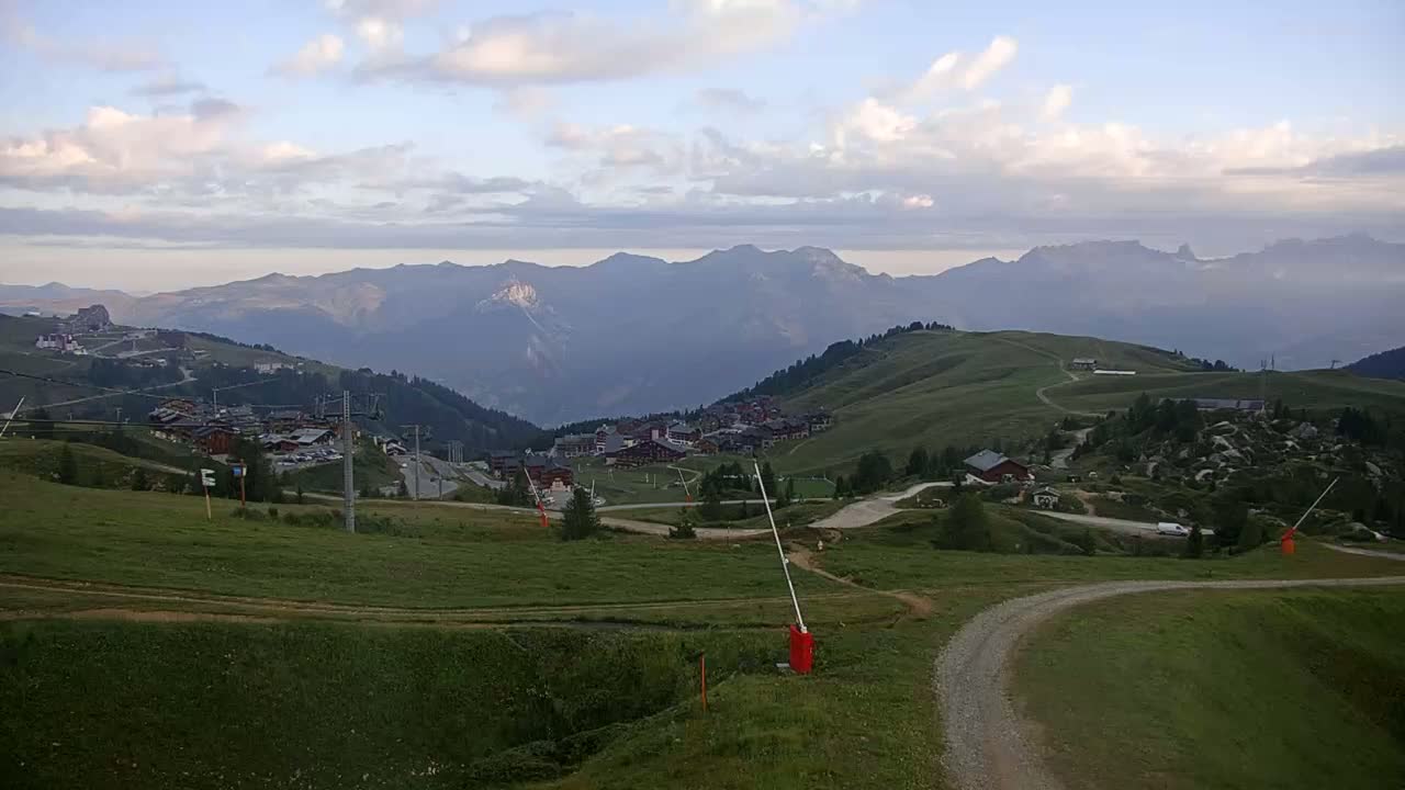 A long, enclosed gondola lift car sits on a grassy hillside under a mostly sunny sky.