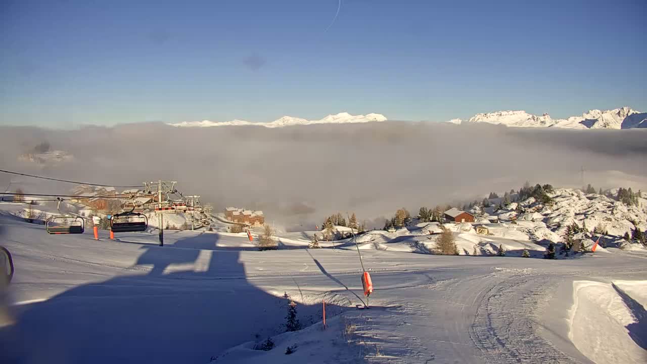 A portion of a gondola car is visible in the foreground, overlooking a grassy mountainside with distant, rocky peaks under a clear, sunny sky.