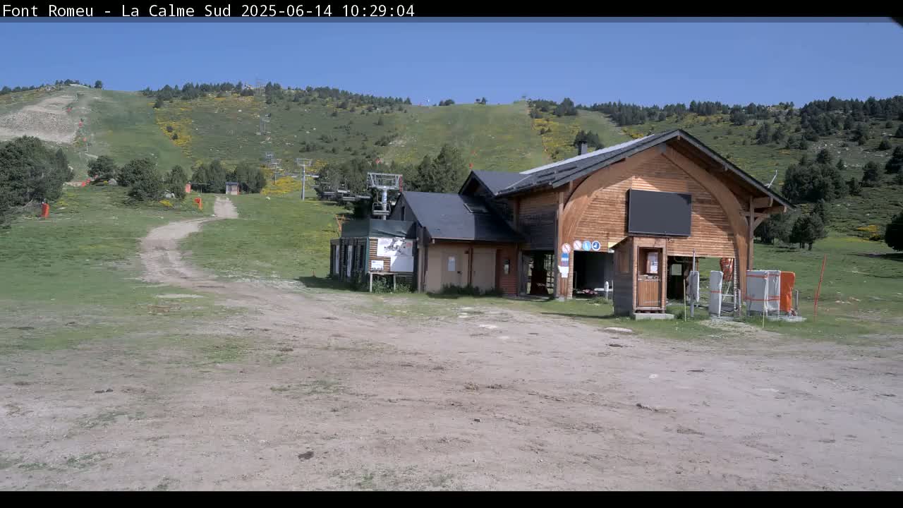 A dirt path leads to a wooden ski lift building situated on a grassy hillside under a clear blue sky.