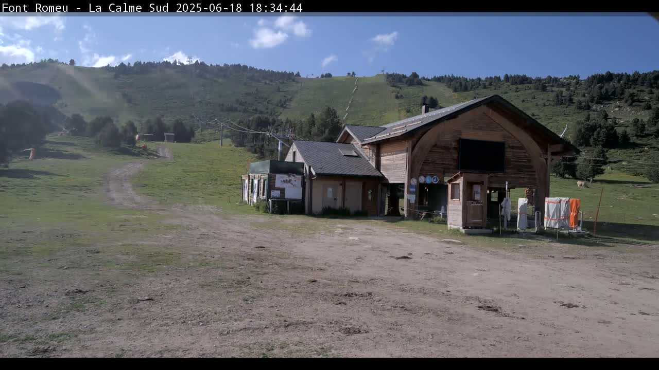 A wooden building sits in a grassy area near a ski lift on a sunny day.