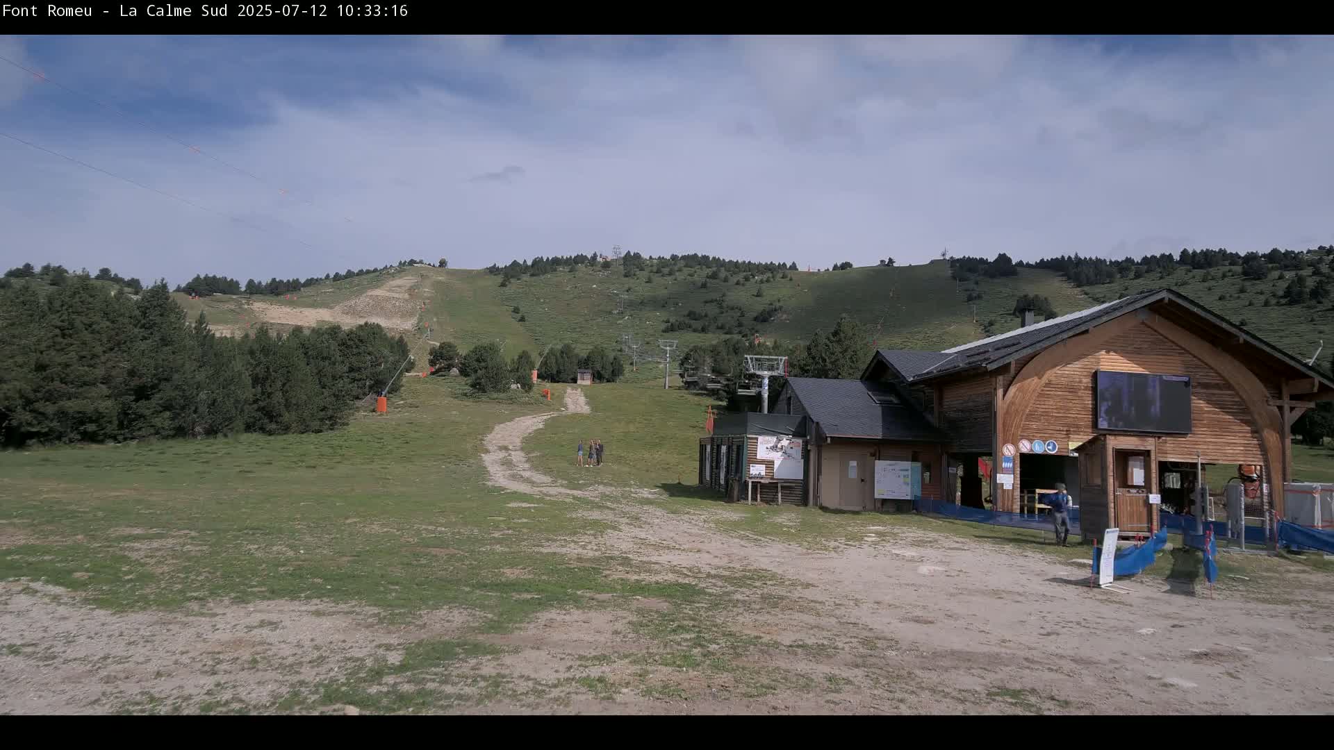 A grassy mountain slope with a ski lift and a wooden building is visible under a partly cloudy sky.