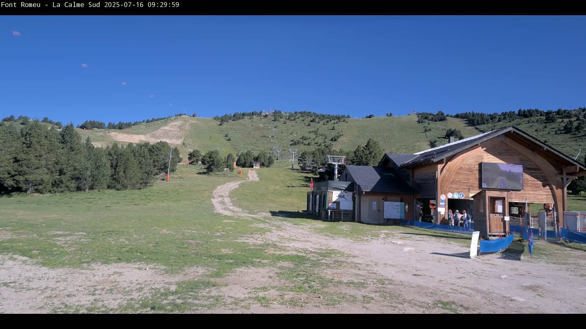 A grassy mountain slope with a chairlift and a wooden building is visible under a clear blue sky.