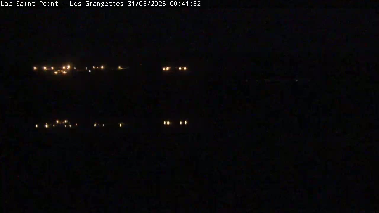 A nighttime, dark scene shows a few distant lights scattered across a landscape.