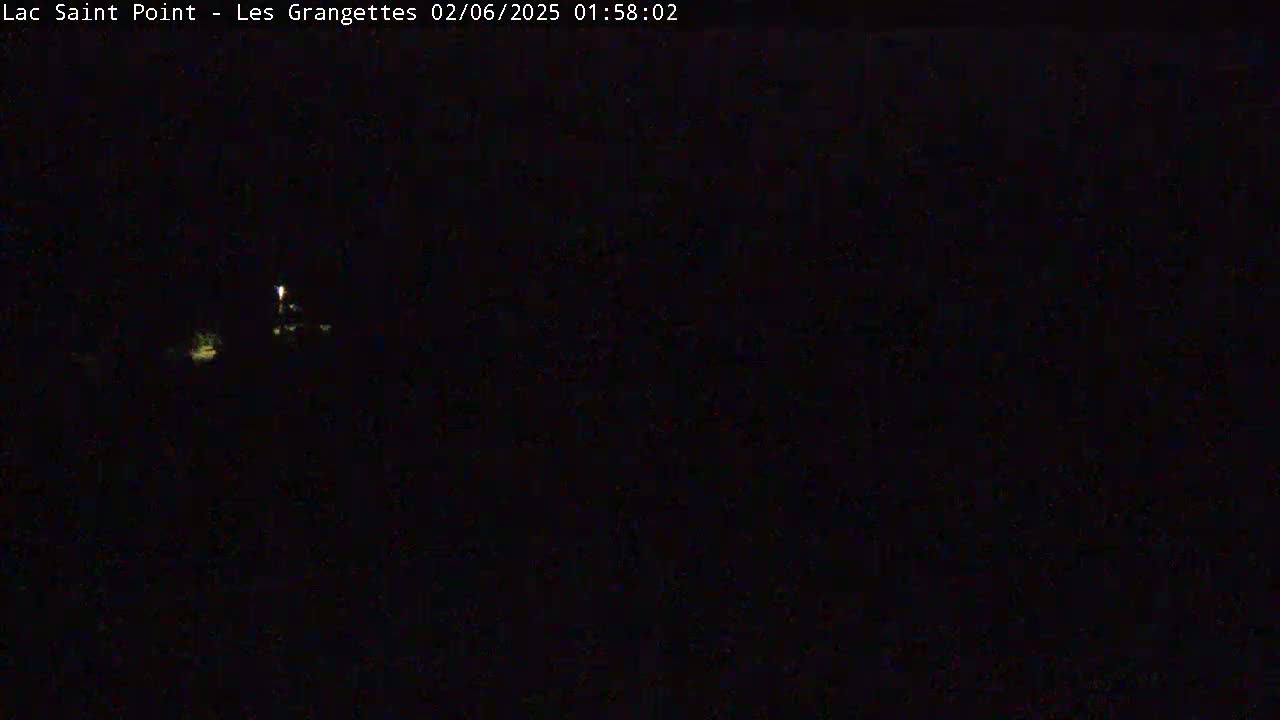 A nighttime, dark image shows a dimly lit area with a few small lights visible in the distance.