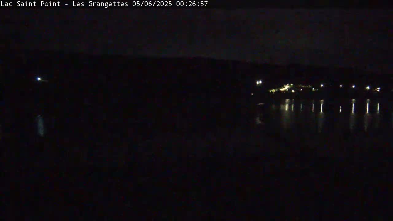 A dark, nighttime view of a body of water reflecting the lights of a distant shoreline under a clear sky.