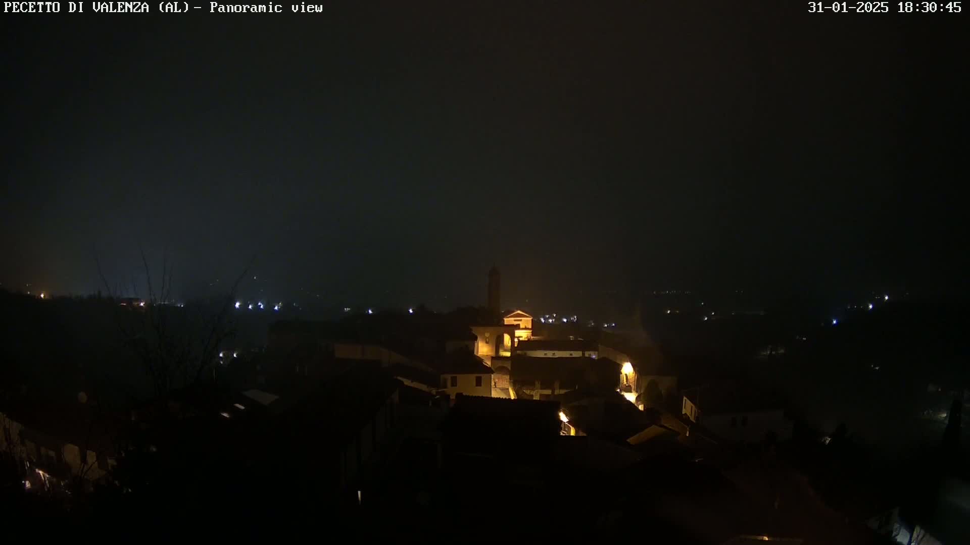 A nighttime panoramic view of a small, dimly lit town under a dark, hazy sky.