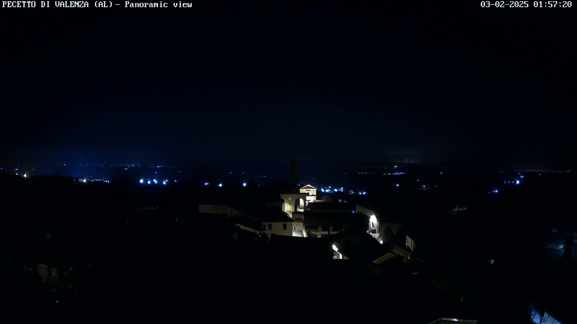 A nighttime panoramic view of a small town illuminated with scattered lights, under a dark, clear sky.