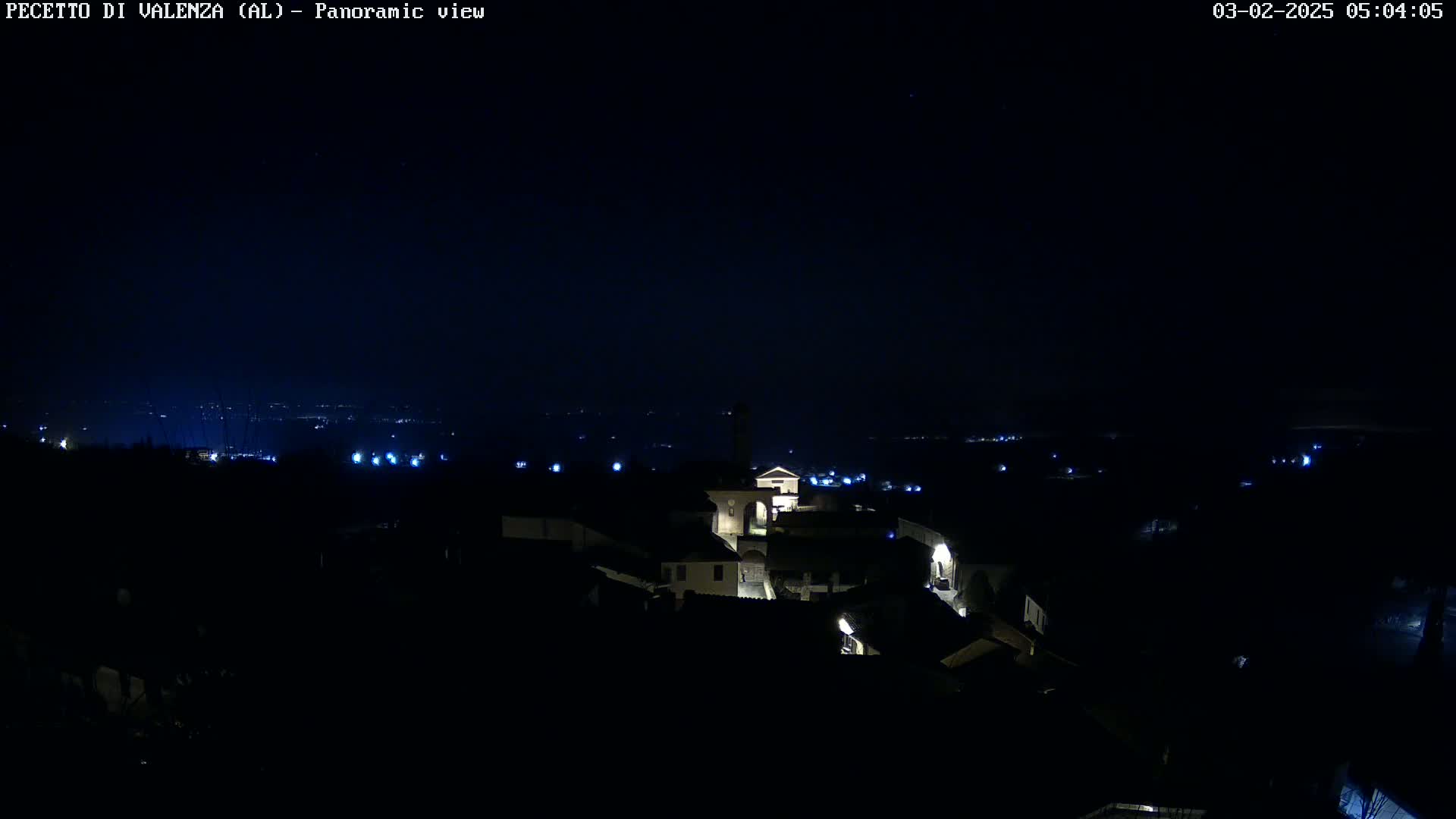 A nighttime panoramic view shows a small town with dimly lit buildings under a clear, dark sky.