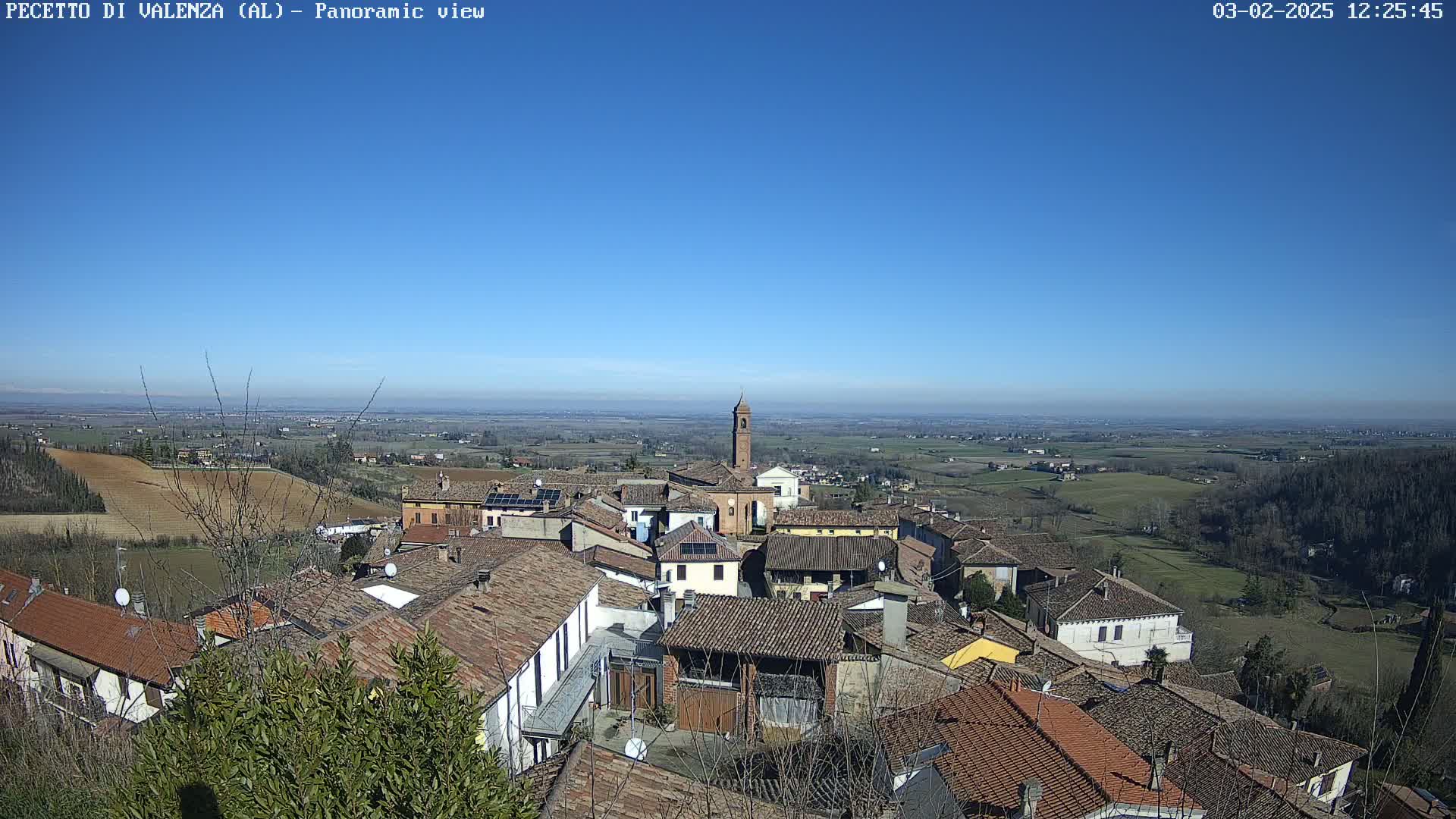 A panoramic view of a small town nestled in a gently rolling landscape under a clear blue sky.