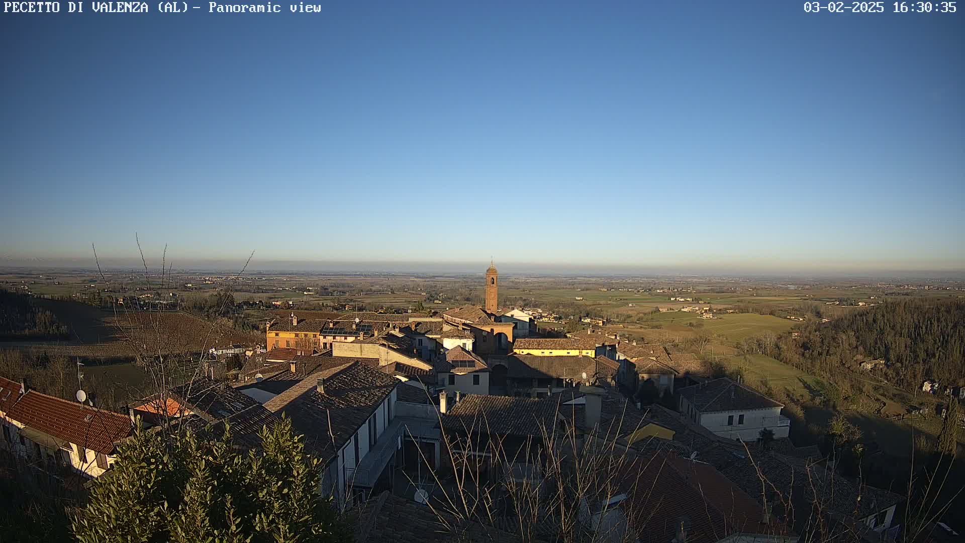 A panoramic view of a small town nestled in a valley under a clear blue sky, with surrounding farmland stretching to the horizon.