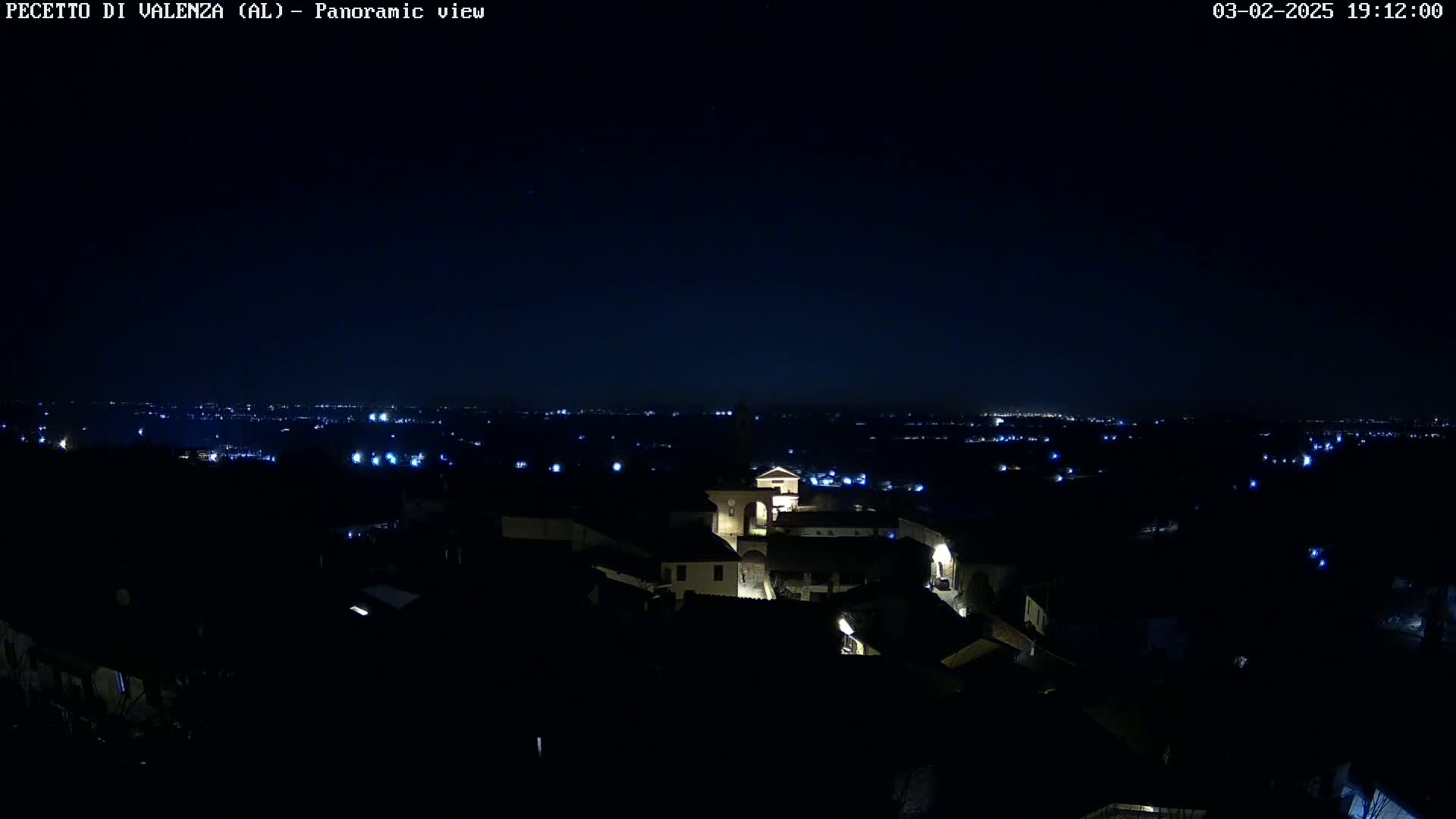 A nighttime panoramic view shows a small town illuminated by scattered lights against a dark, clear sky.