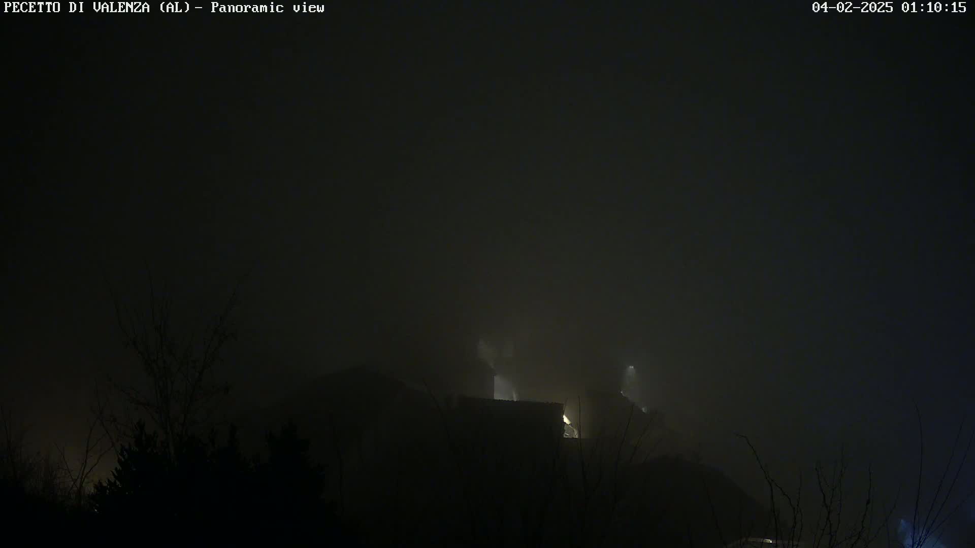 A foggy night scene shows dimly lit buildings atop a hill obscured by darkness and fog.