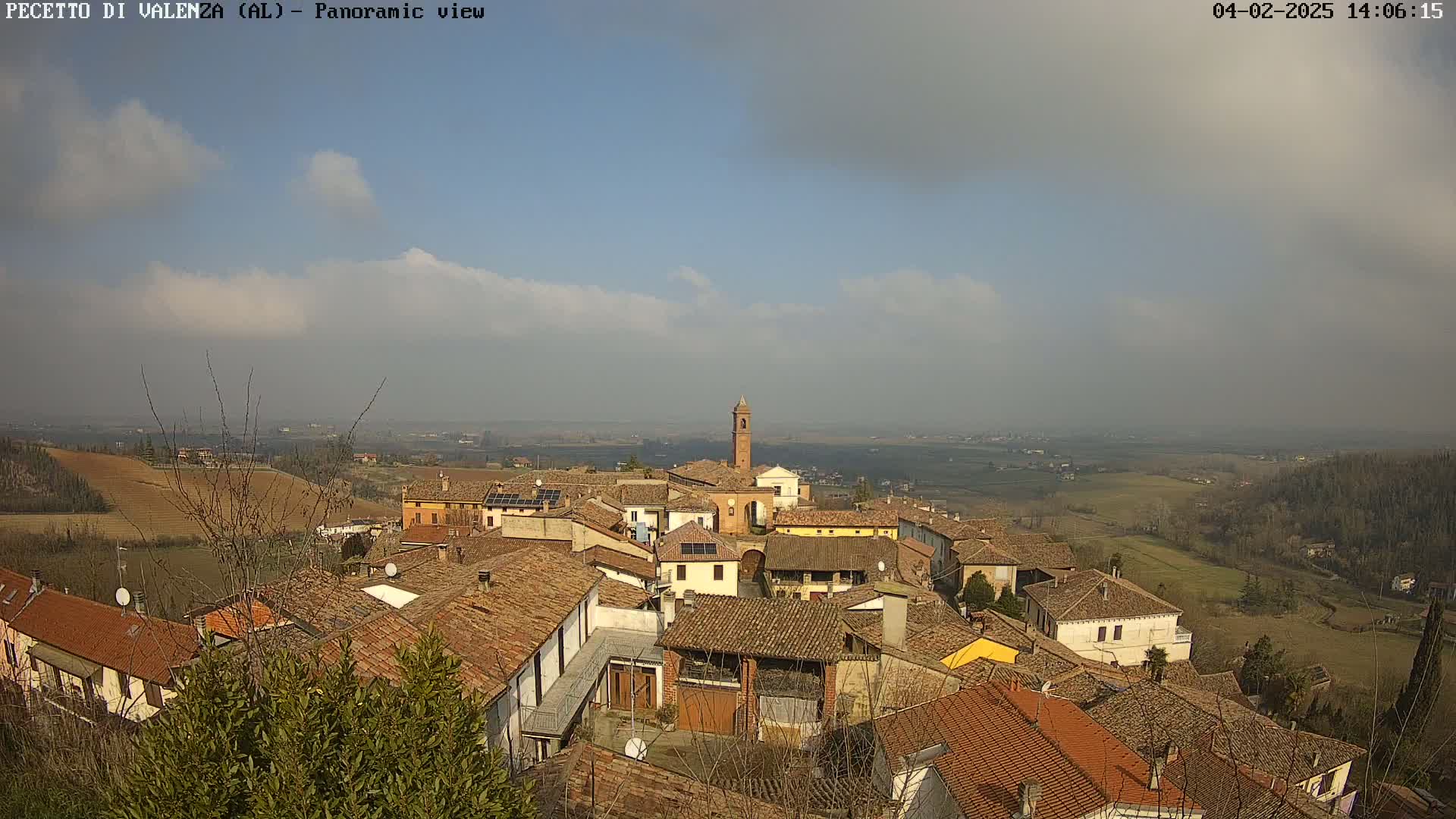 A panoramic view of a small town with terracotta roofs, under a partly cloudy sky.