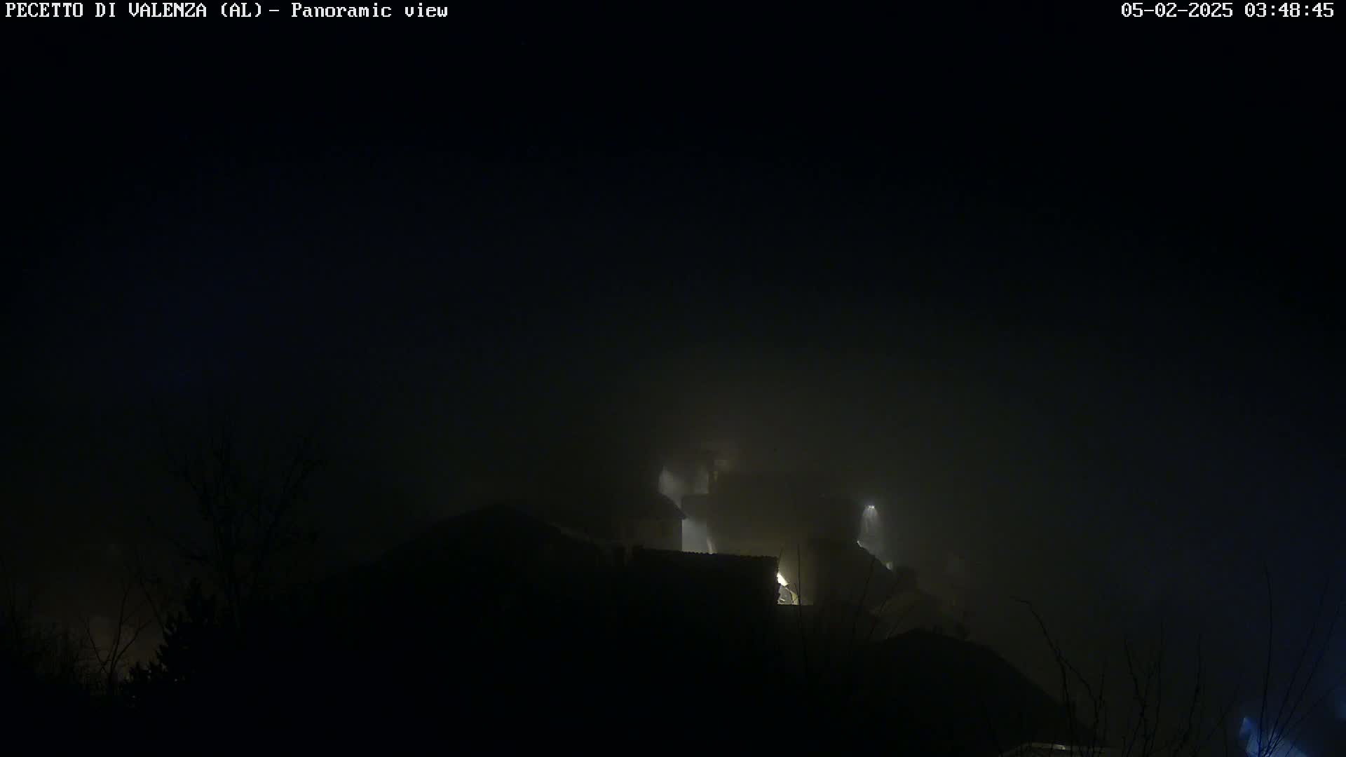 A foggy, nighttime scene shows dimly lit buildings nestled in the hills.