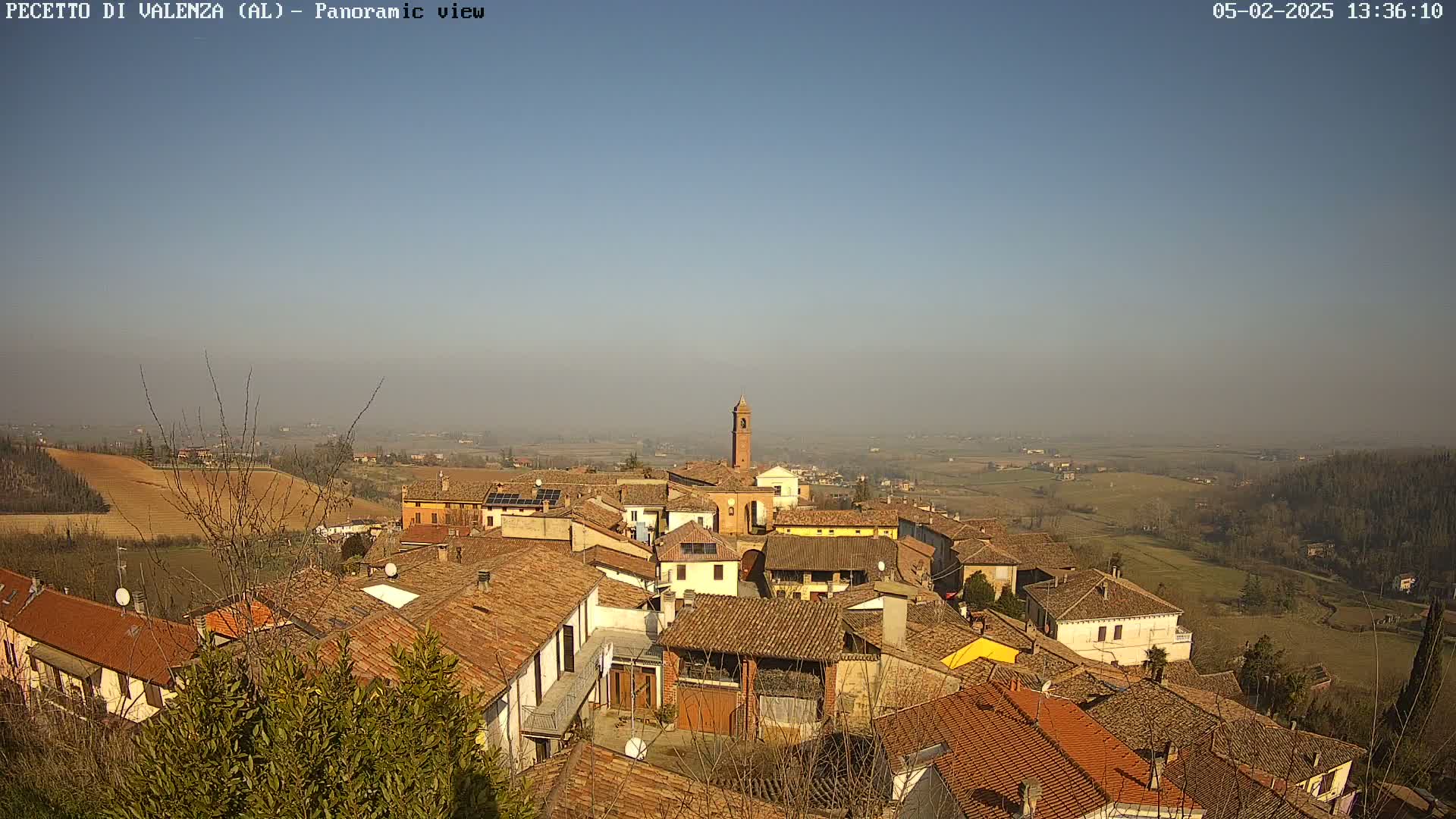 A panoramic view of a small town with terracotta rooftops under a clear, hazy sky.