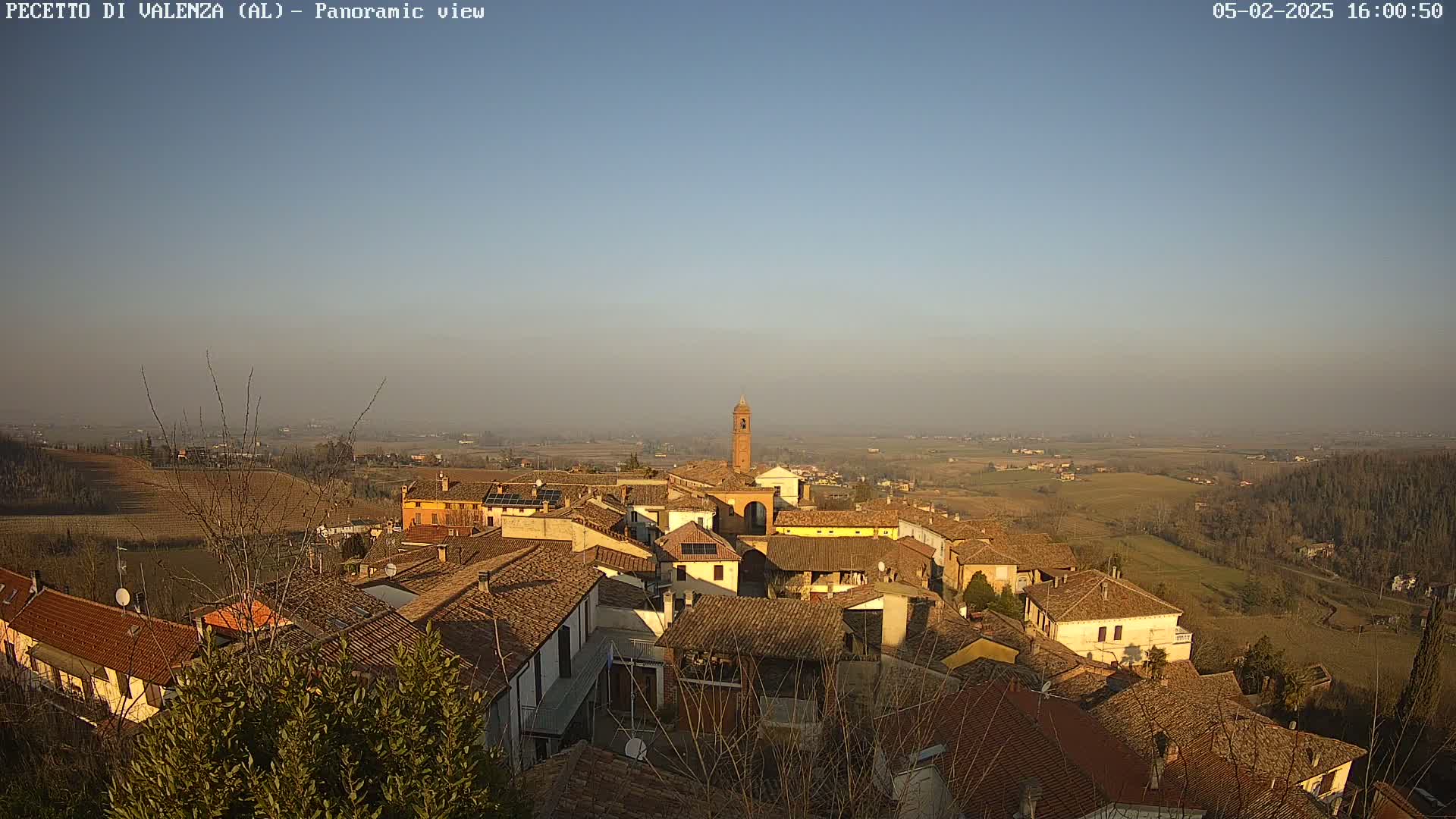 A panoramic view of a small town nestled in a hilly landscape under a clear, hazy sky.