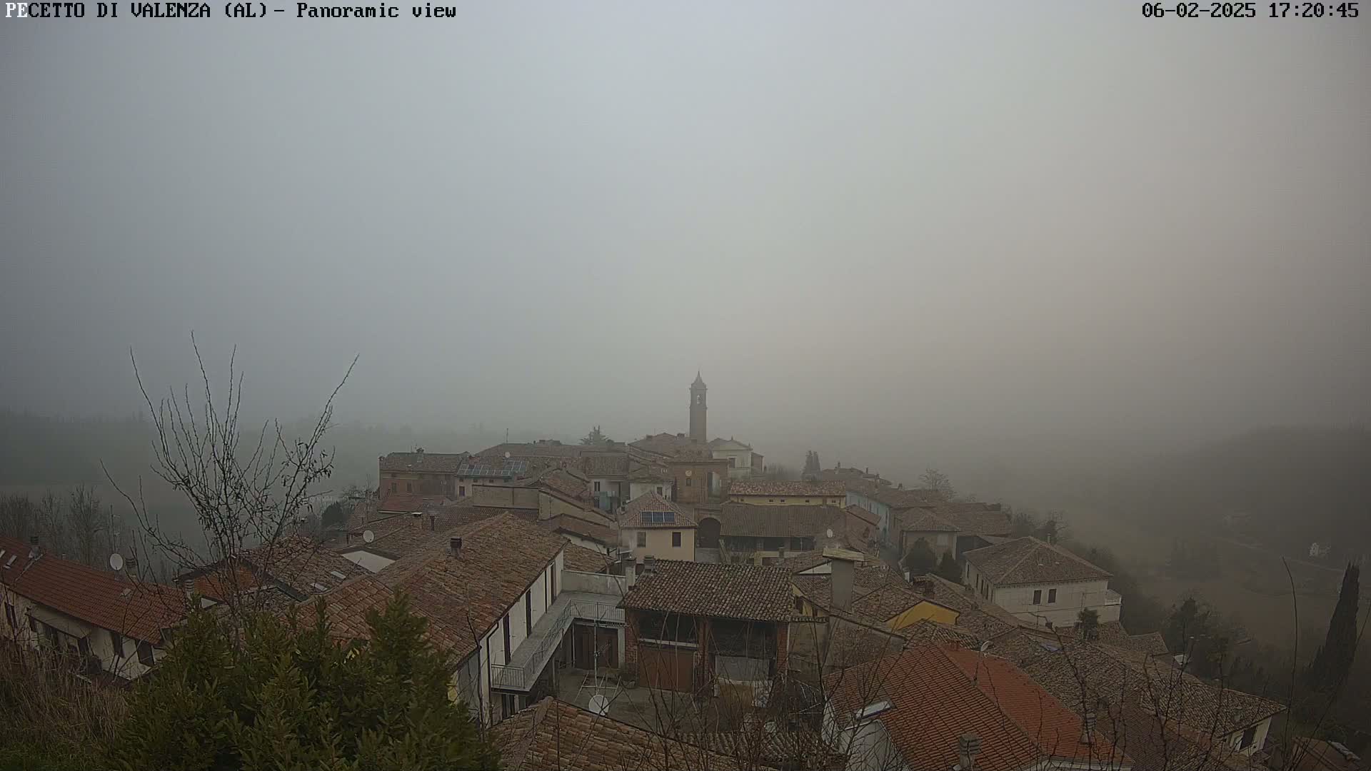A foggy view overlooks a village of brown-roofed buildings, with a tall bell tower visible in the center.