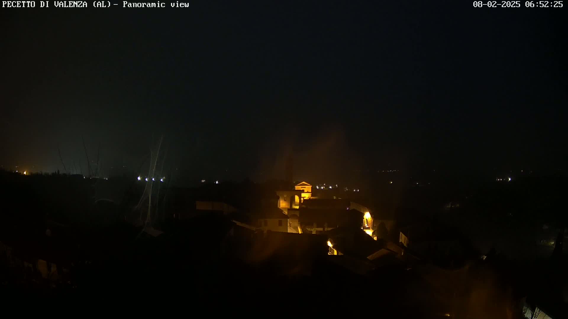 A nighttime panoramic view of a small town nestled in a valley, dimly lit with a hazy or foggy atmosphere.