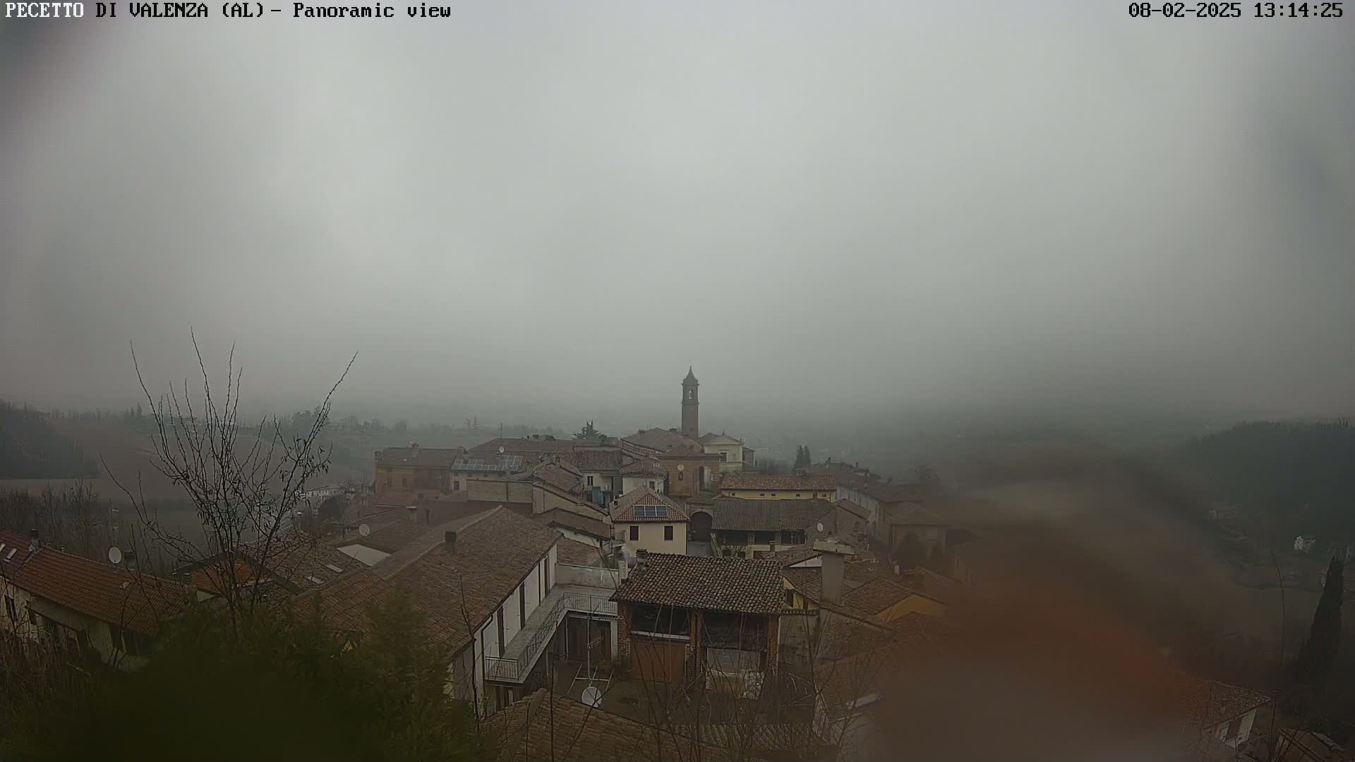 A foggy view of a small town with red tile roofs and a tall bell tower in the center.