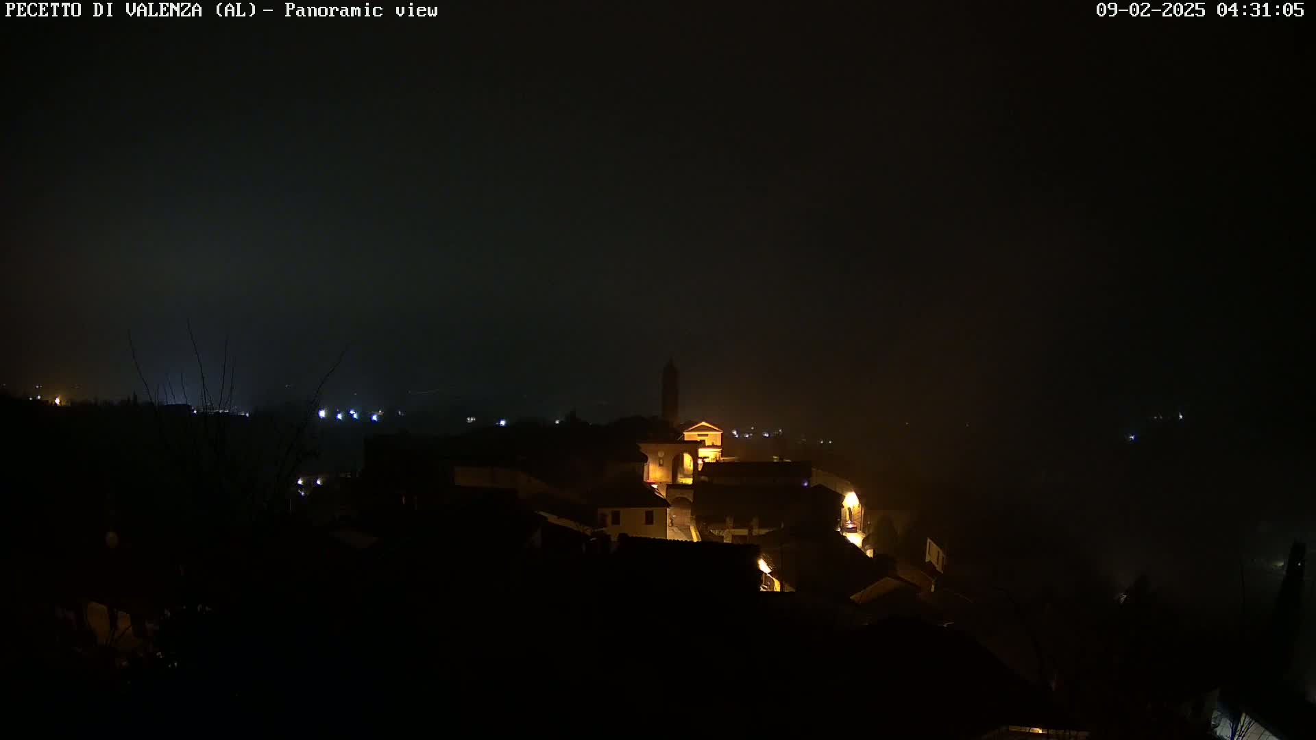 A nighttime panoramic view of a small, dimly lit town shrouded in fog.