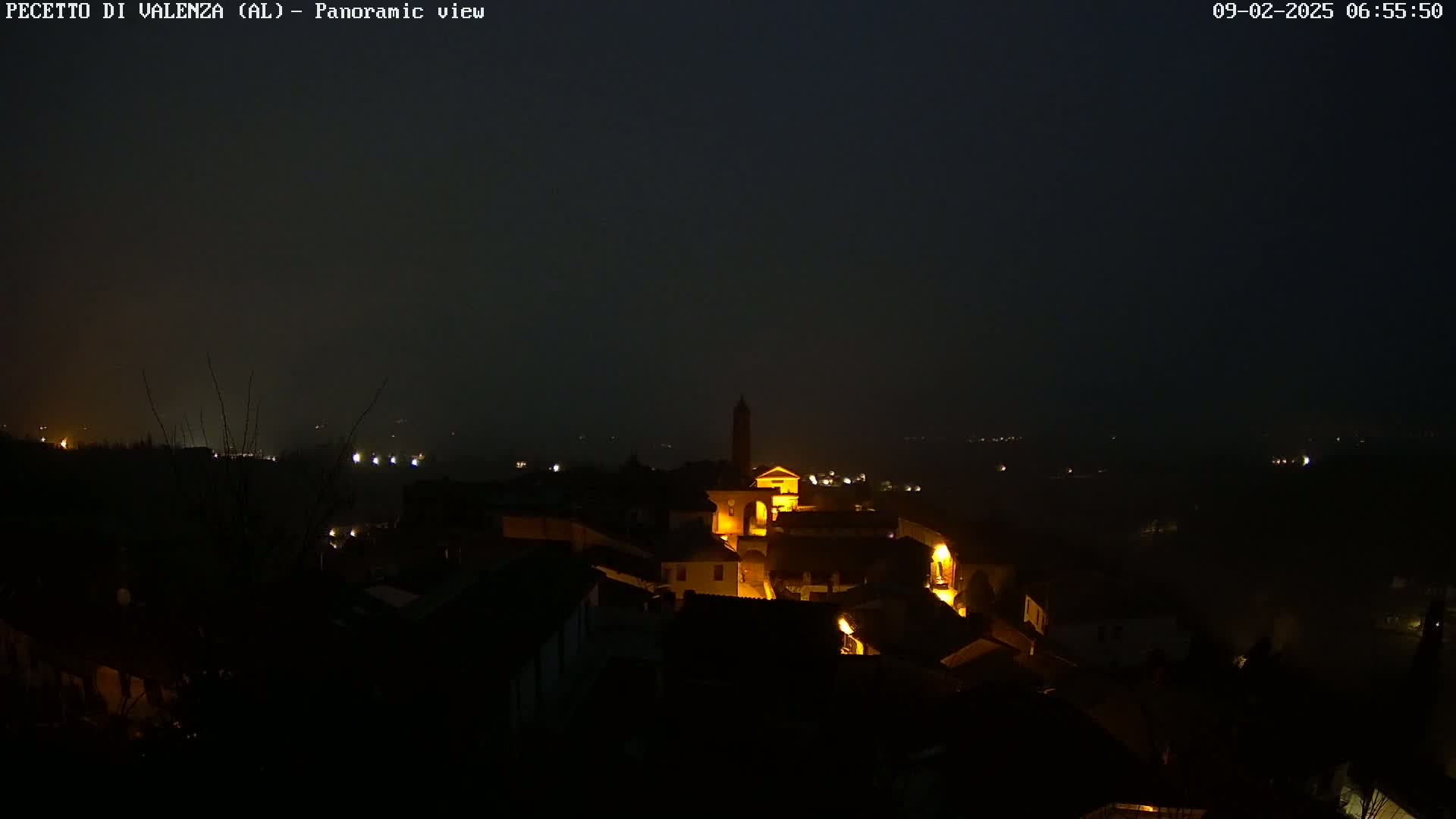A nighttime panoramic view of a small town nestled in a valley under a dark, hazy sky.