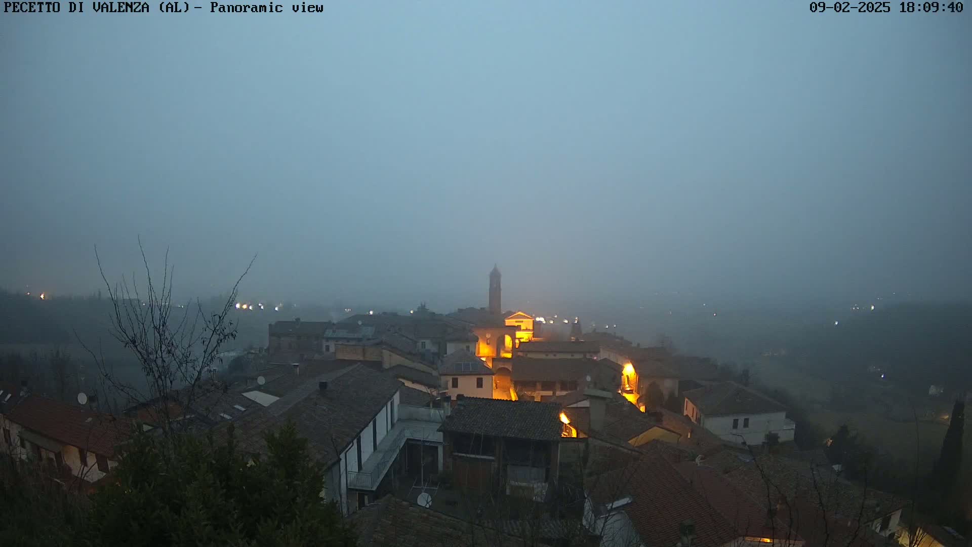 A foggy, dimly lit town at dusk, with the lights of buildings visible through the haze.