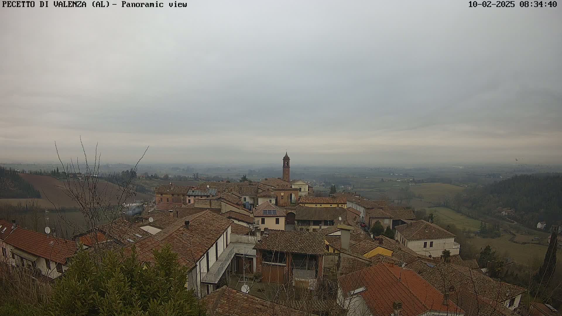 A panoramic view of a town with red-tiled roofs and a bell tower under an overcast sky.