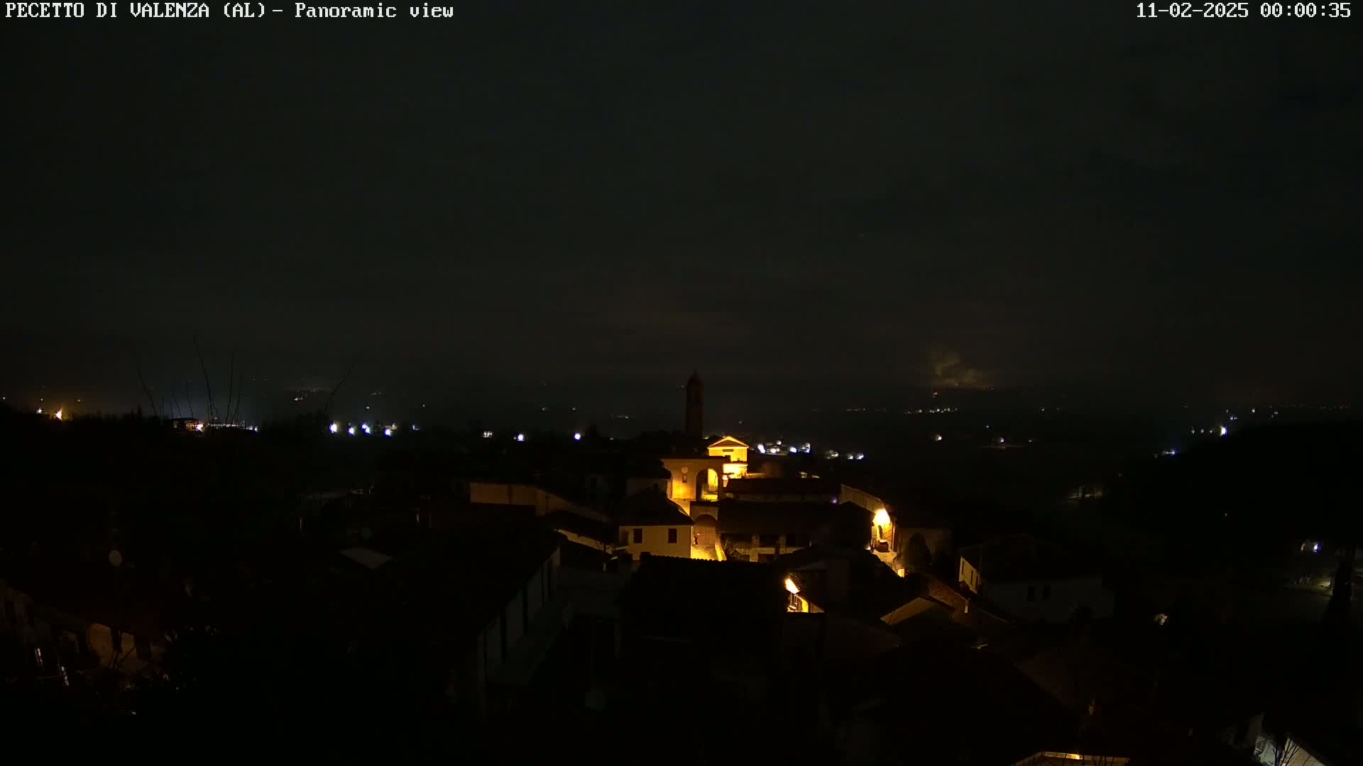 A nighttime panoramic view of a small, dimly lit town nestled in a valley under a dark, cloudy sky.