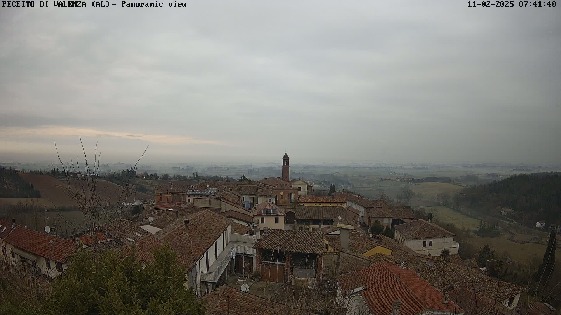 A panoramic view of a small town nestled in a hilly landscape under a hazy, overcast sky.