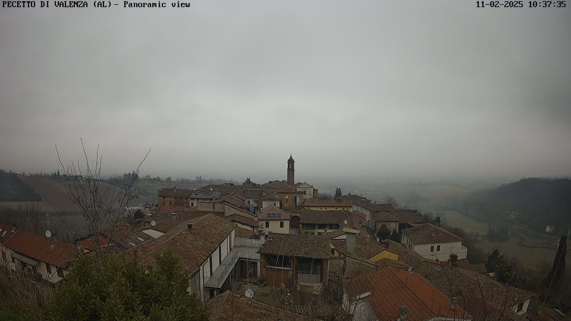 A small town with red-tiled roofs and a tall bell tower is visible under a hazy, overcast sky.