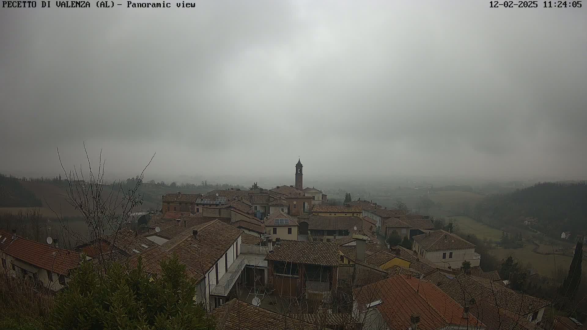 A hazy, overcast view overlooks a small town of brown-roofed buildings nestled in a valley.