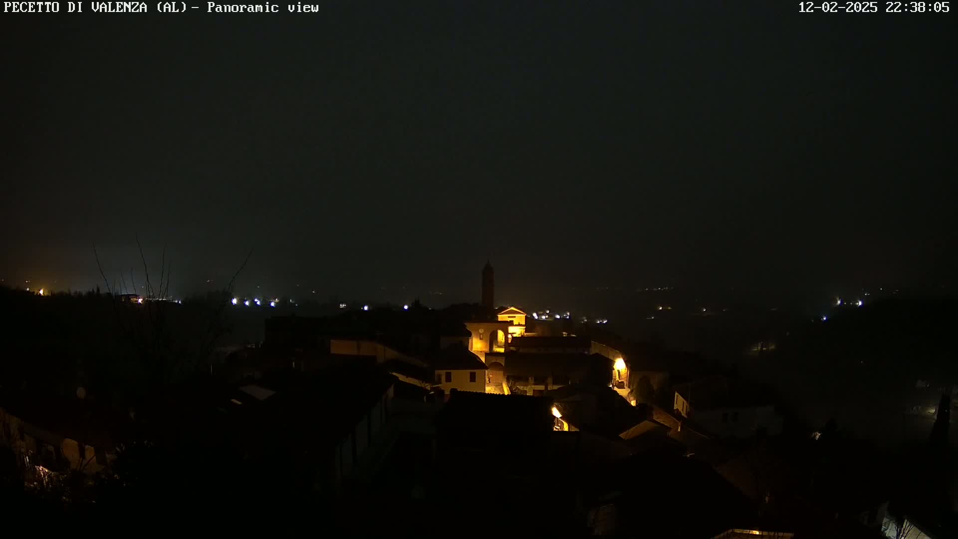 A nighttime panoramic view of a small town nestled in a valley shrouded in fog or mist.