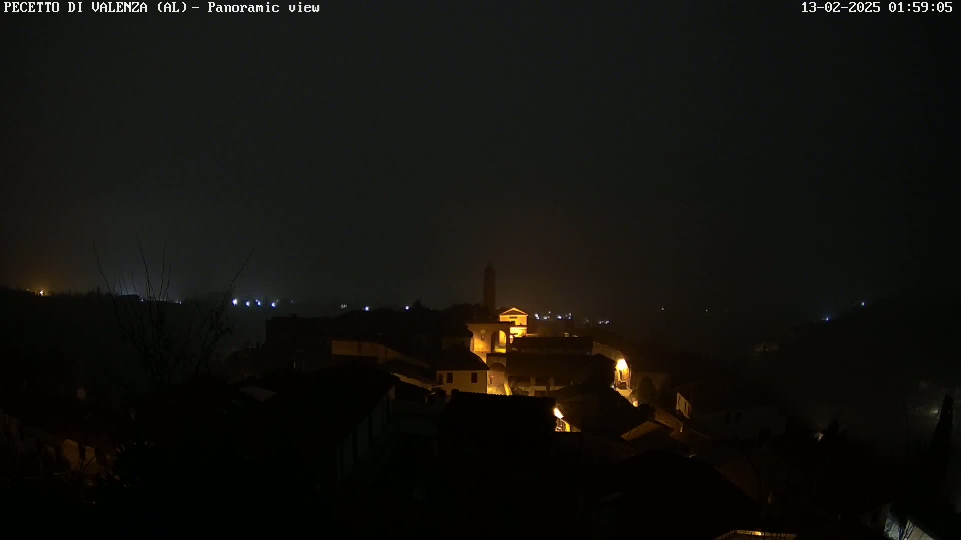 A foggy, nighttime view of a small town nestled in a hillside, with a few lights illuminating buildings.