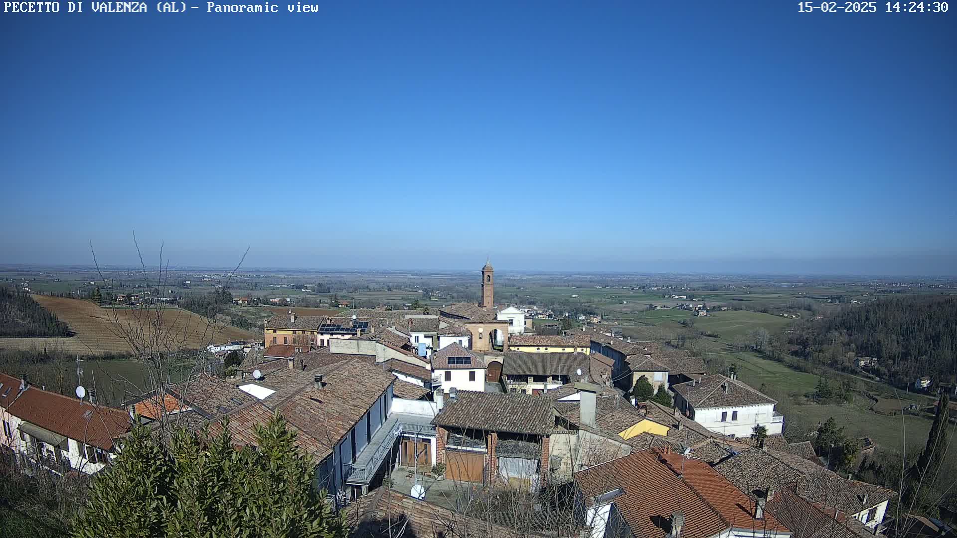 A panoramic view of a village with red tile roofs under a clear blue sky shows a vast, flat landscape stretching to the horizon.