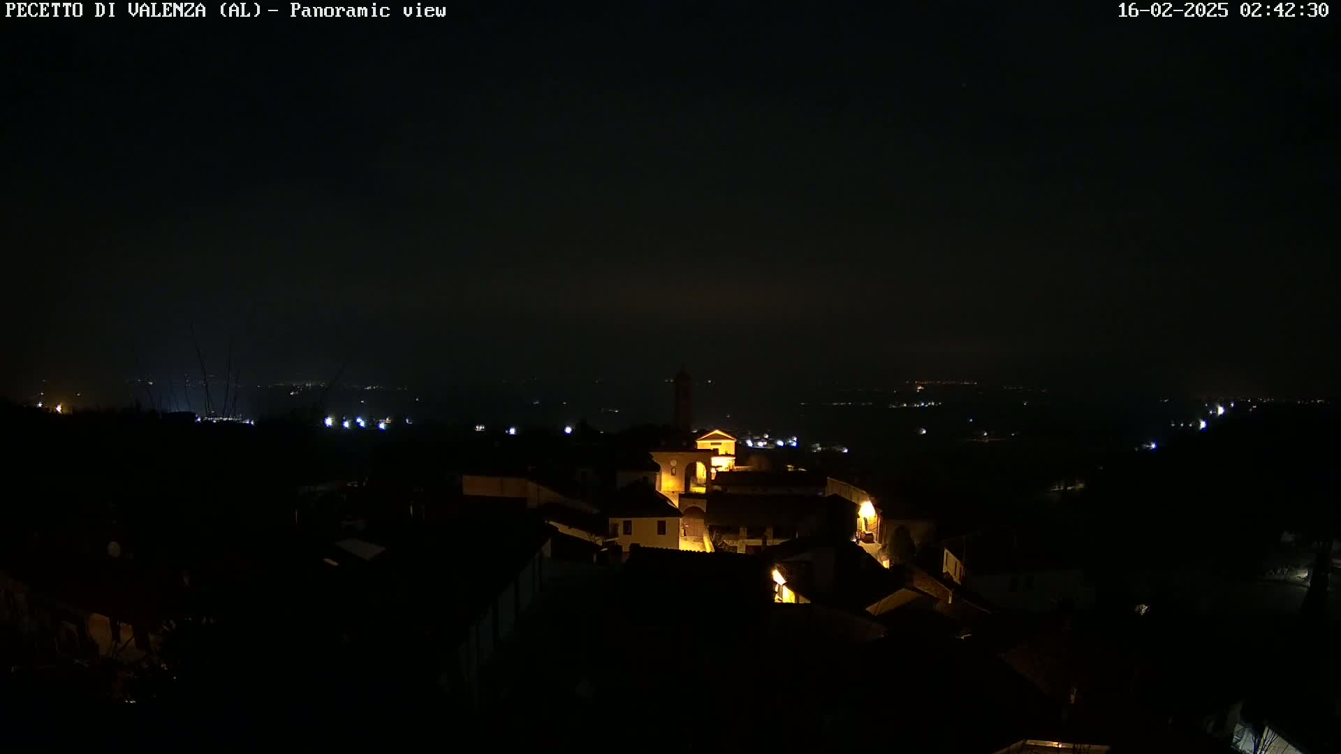 A nighttime panoramic view shows a small town with dimly lit buildings under a dark, clear sky.
