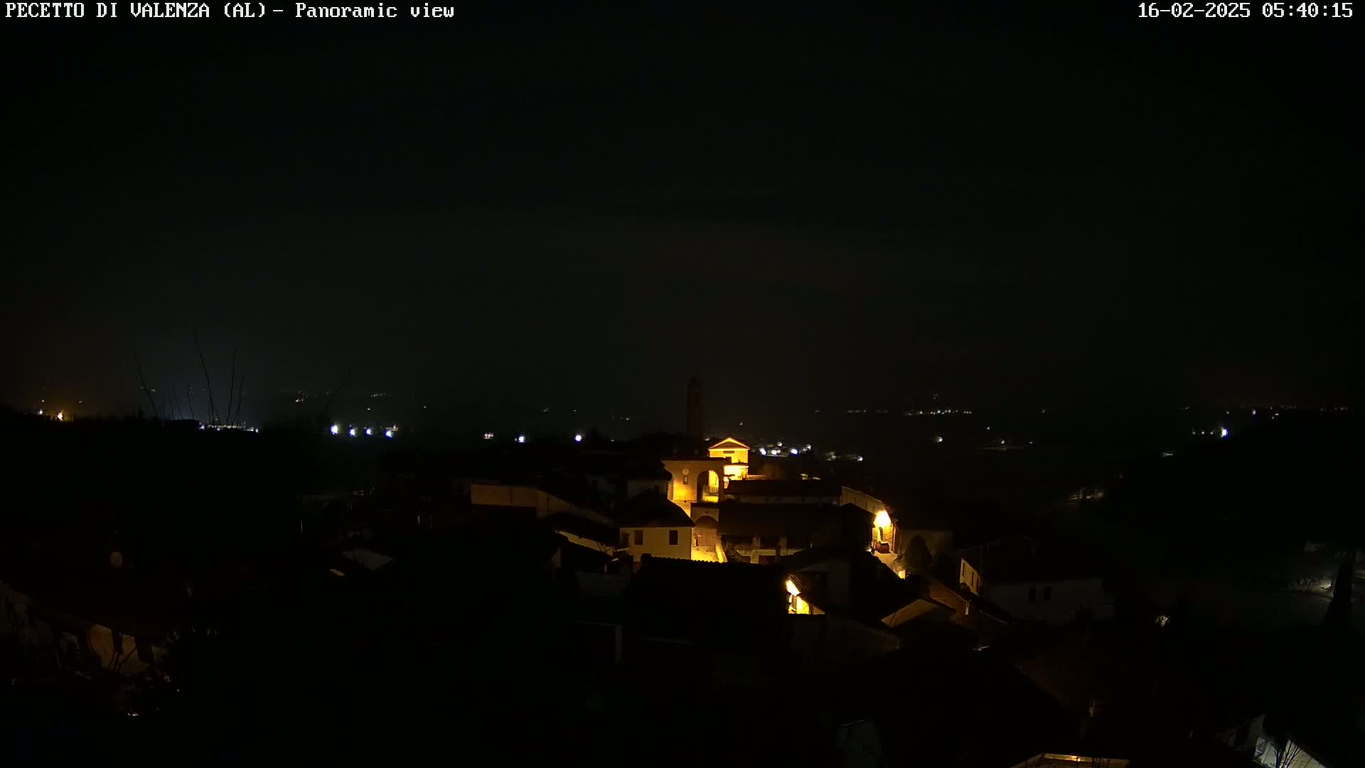 A nighttime panoramic view of a small, dimly lit town nestled in a dark landscape under a clear, dark sky.