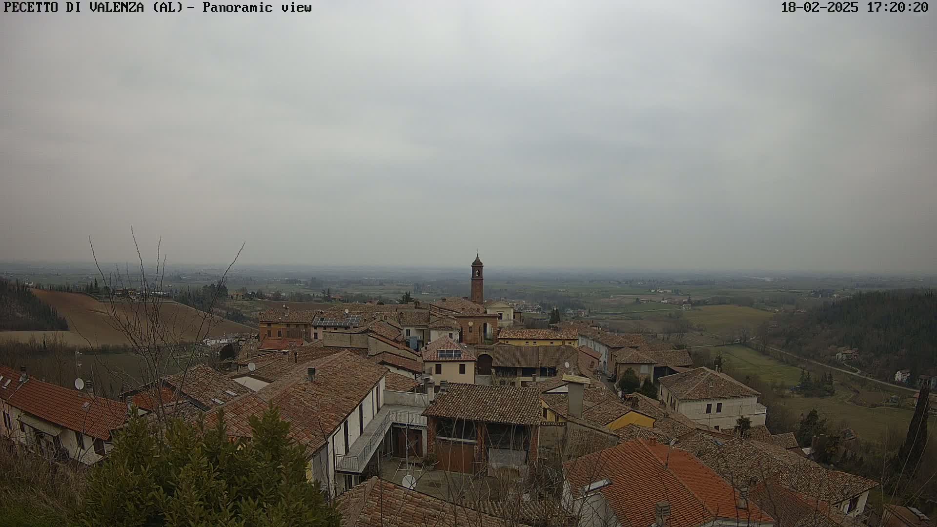 A panoramic view of a town with red-tiled roofs under an overcast sky shows a flat landscape stretching into the distance.