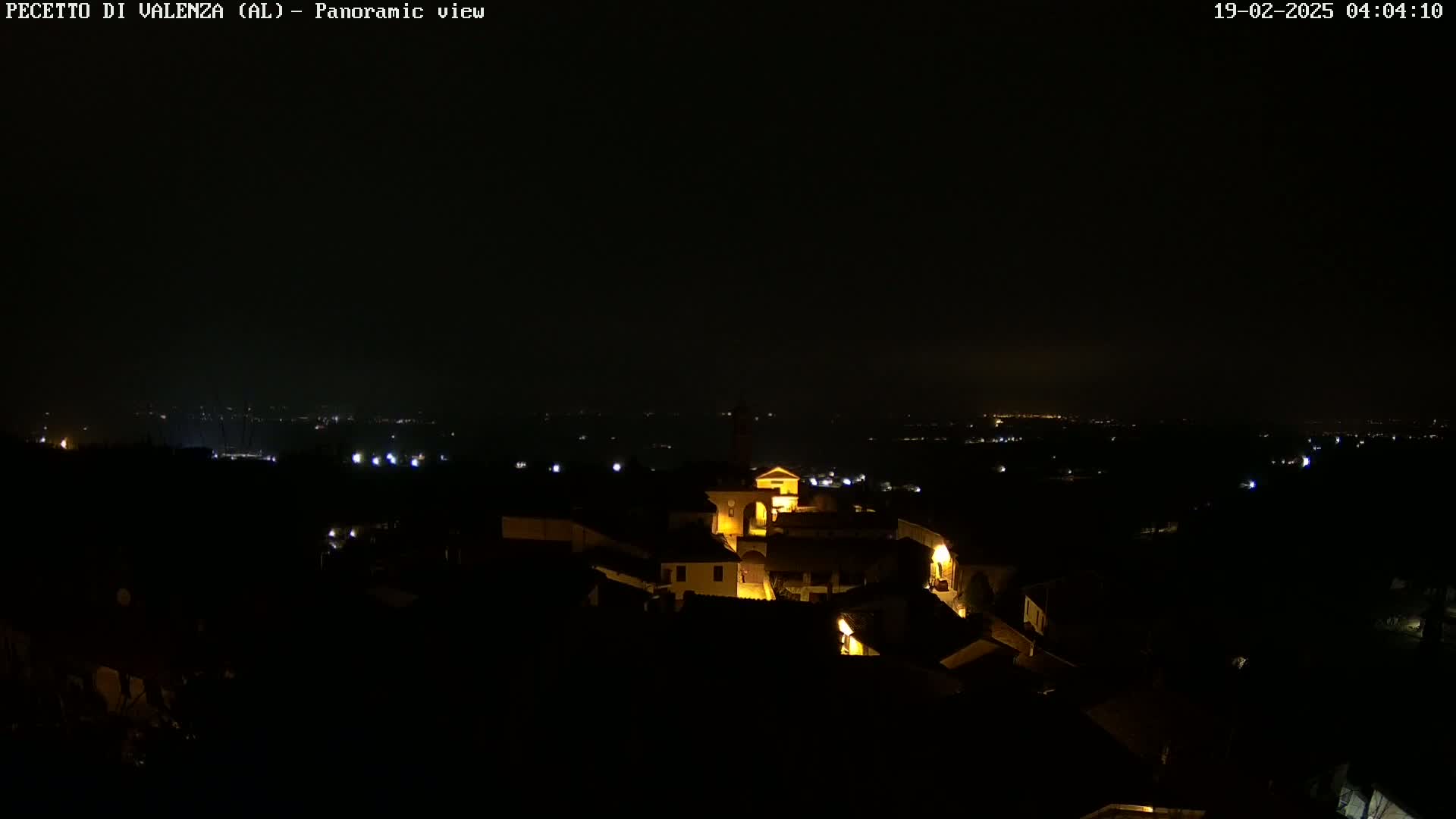 A nighttime, panoramic view of a small, illuminated town nestled in a dark landscape under a clear sky.