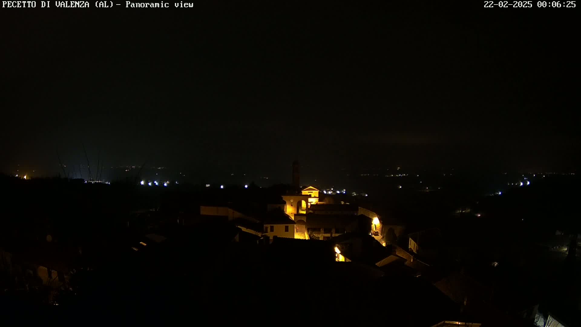 A small, dimly lit town is nestled in a dark landscape under a night sky.