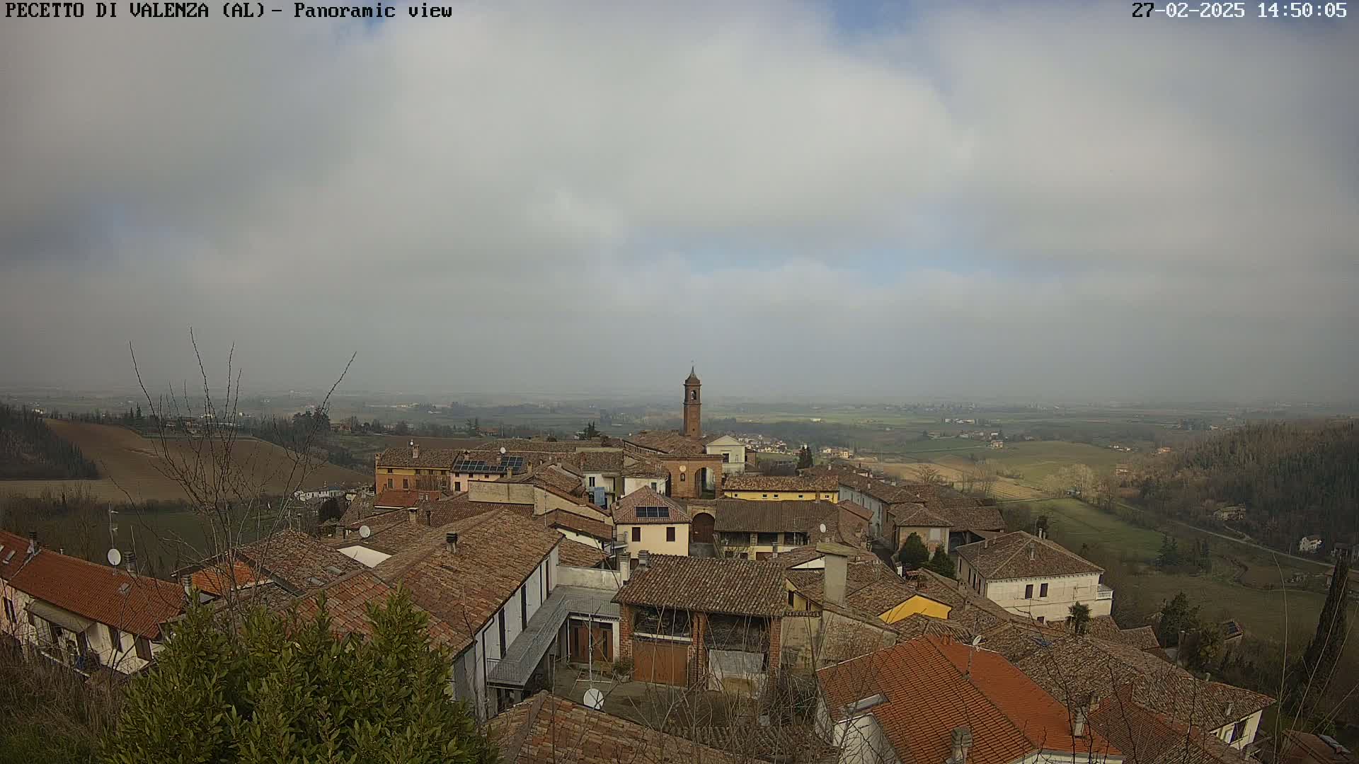 A panoramic view of a small town with red-tiled roofs, under a mostly cloudy sky.