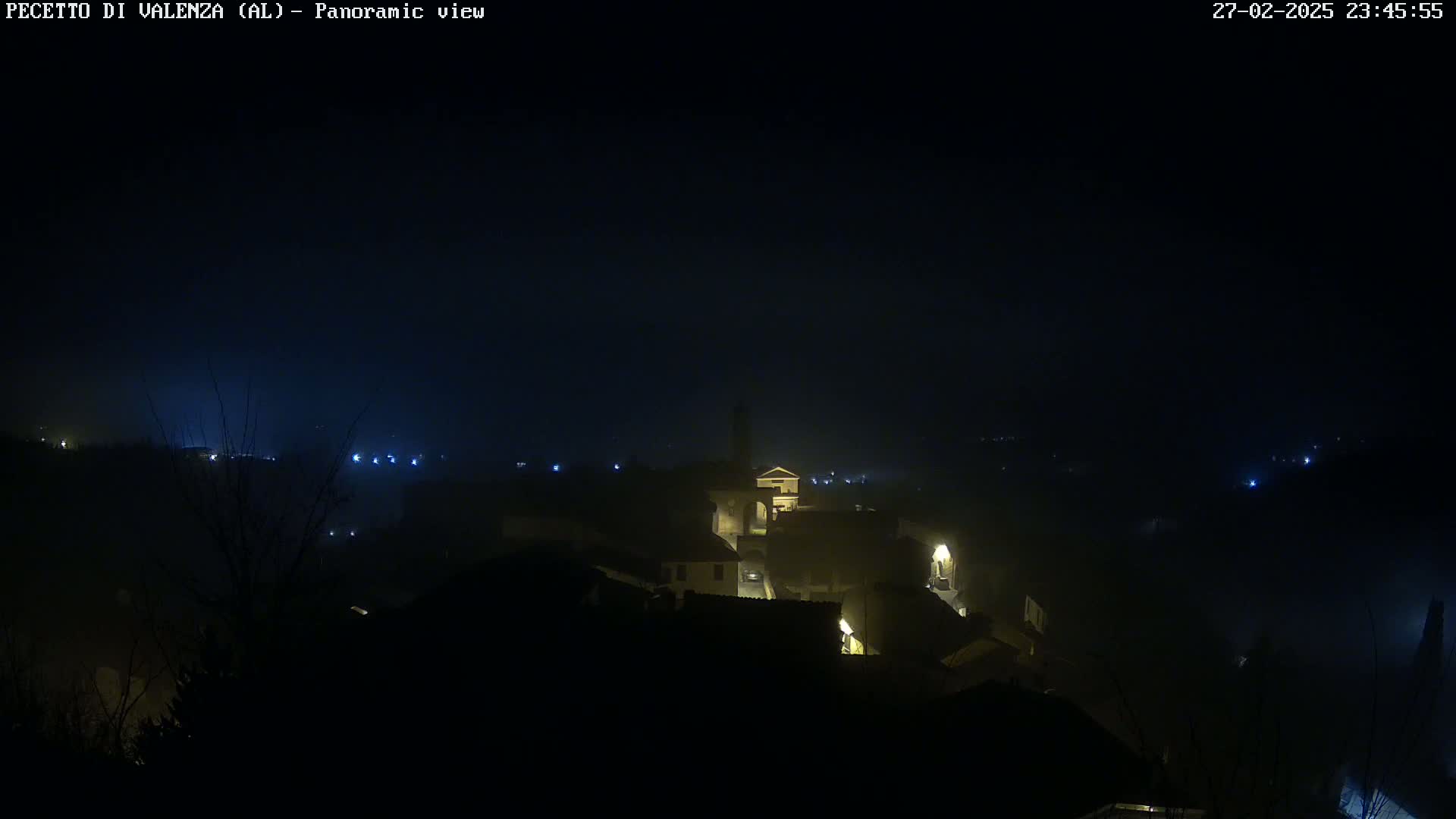 A foggy, nighttime panoramic view of a dimly lit town with a few lights visible.