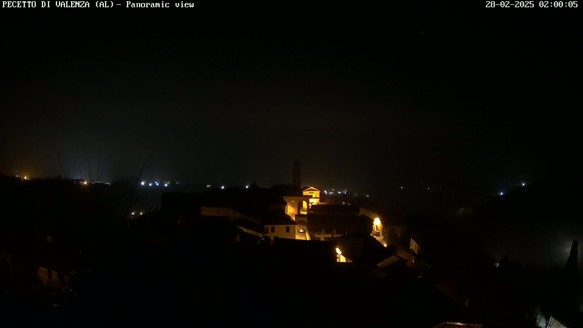 A nighttime panoramic view of a dimly lit village under a foggy, dark sky.