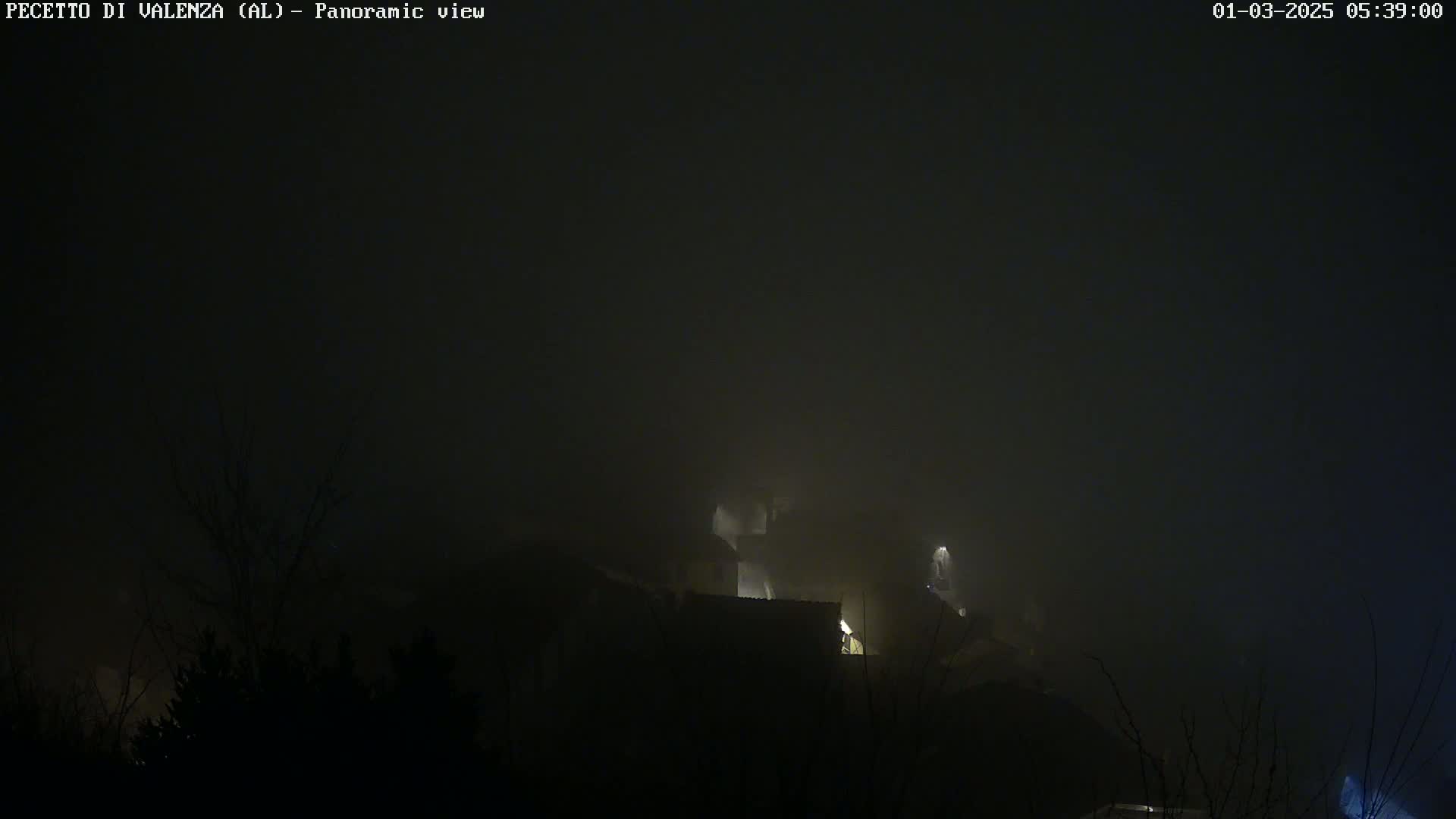 A foggy, nighttime scene shows dimly lit buildings partially obscured by heavy fog.