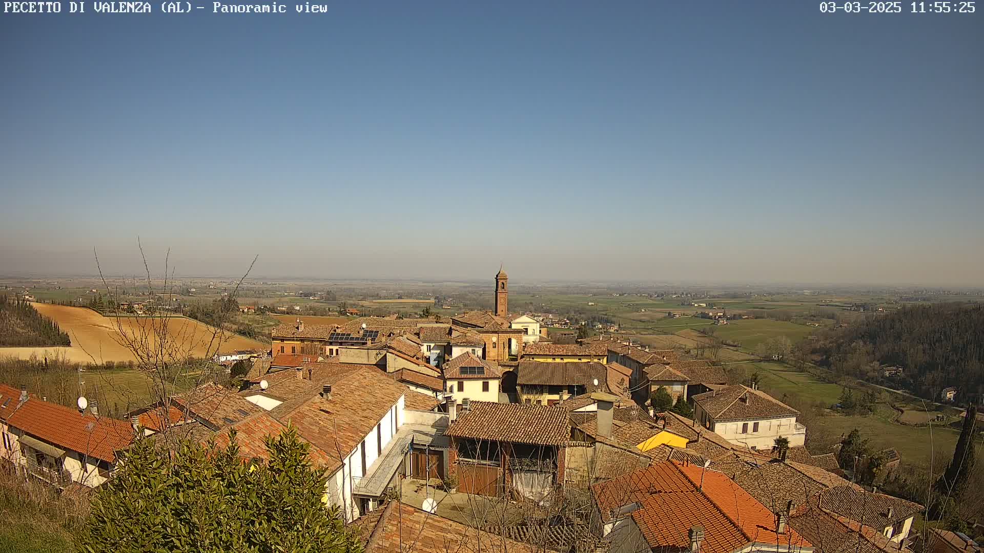 A panoramic view of a village nestled in a valley on a clear, sunny day, with expansive farmland stretching out to the horizon.