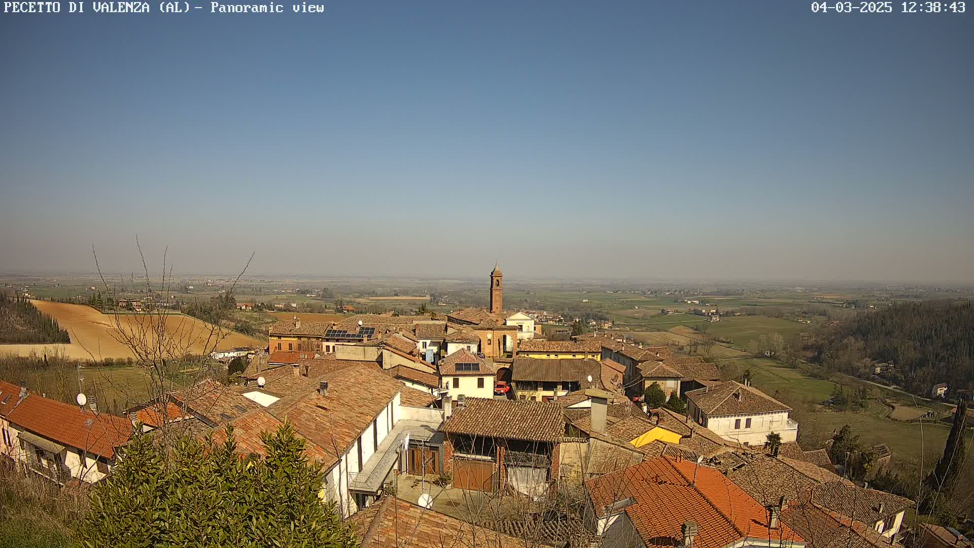 A panoramic view of a small town nestled in a valley on a clear, sunny day, with rolling hills and farmland stretching into the distance.